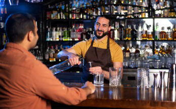 Barman préparant un cocktail avec un doseur face à un client.