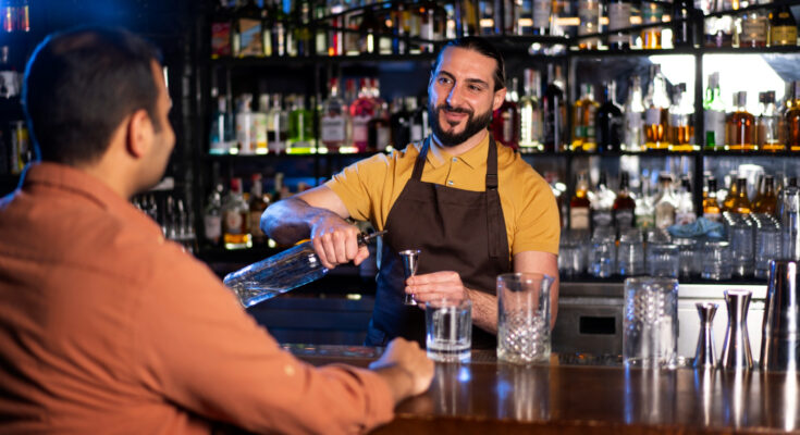 Barman préparant un cocktail avec un doseur face à un client.