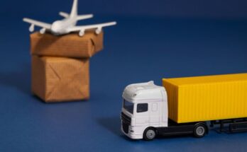 Une miniature de camion blanc à remorque jaune et un petit avion blanc posé sur des paquets en carton, symbolisant la logistique et le transport international sur fond bleu.