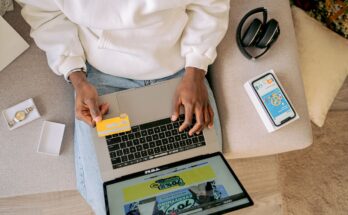 une personne vue du dessus, installée sur un canapé, utilisant sa carte bancaire et son ordinateur portable pour effectuer des achats en ligne