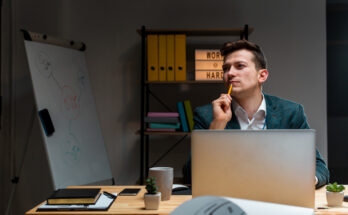 un jeune entrepreneur ou professionnel pensif à son bureau, le crayon posé sur le menton en pleine réflexion
