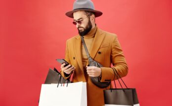 une veste marron et d'un chapeau gris, consultant son smartphone tout en portant plusieurs sacs de shopping
