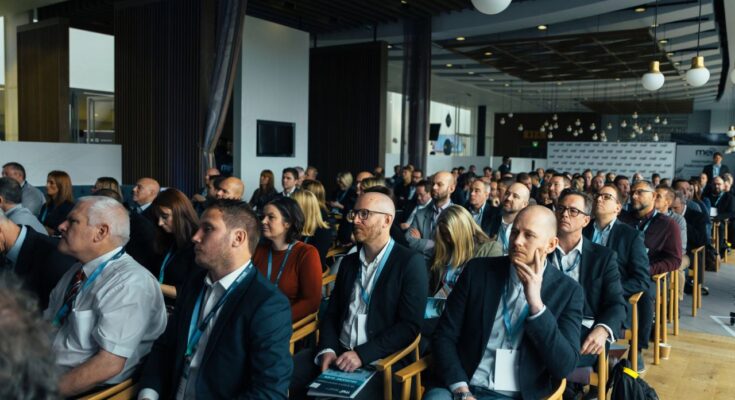 un public attentif assis dans une grande salle de conférence écoutant une présentation lors d'un événement professionnel