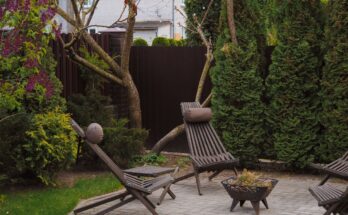 un jardin bordé de verdure, composé de chaises longues en bois, d'un petit braséro en métal et d'un sol pavé