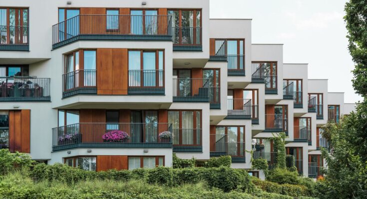 Façade d'un immeuble résidentiel moderne aux balcons décalés avec finitions en bois et éléments végétalisés.