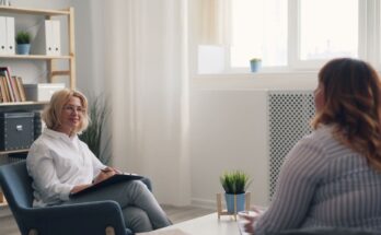 Une thérapeute en blouse blanche écoute attentivement sa patiente lors d'une consultation en cabinet.