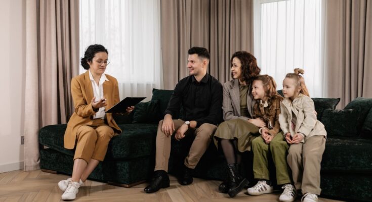 Une conseillère financière échange avec une famille de quatre personnes installée sur un canapé dans un salon moderne